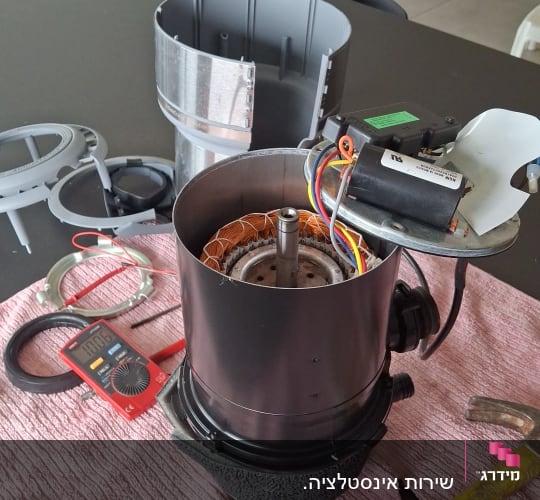 חלקי מכשיר חשמלי מפורקים על שולחן עם כלים